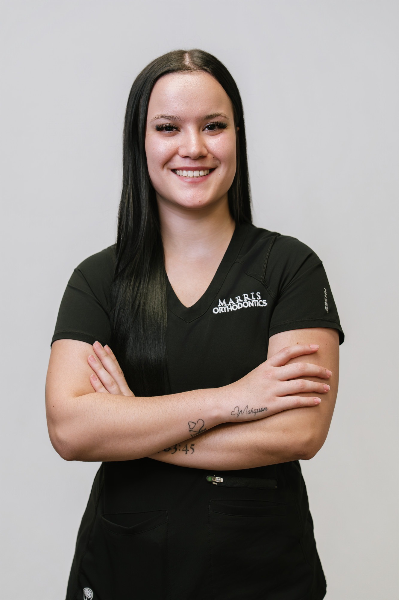 Smiling female orthodontic team member in black scrubs with "Marris Orthodontics" logo, showcasing expertise in braces and Invisalign in Orlando.
