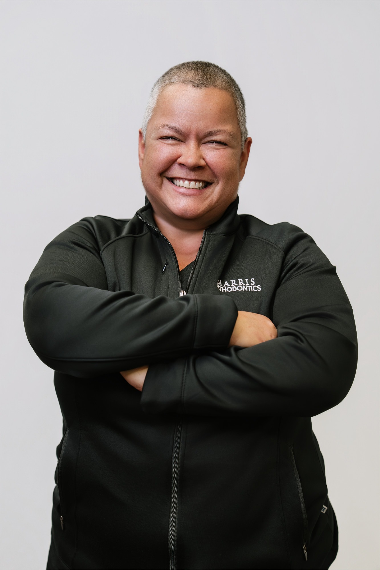 Smiling female practice administrator at Marris Orthodontics, wearing a branded black jacket, arms crossed, showcasing commitment to patient care in Orlando orthodontics.