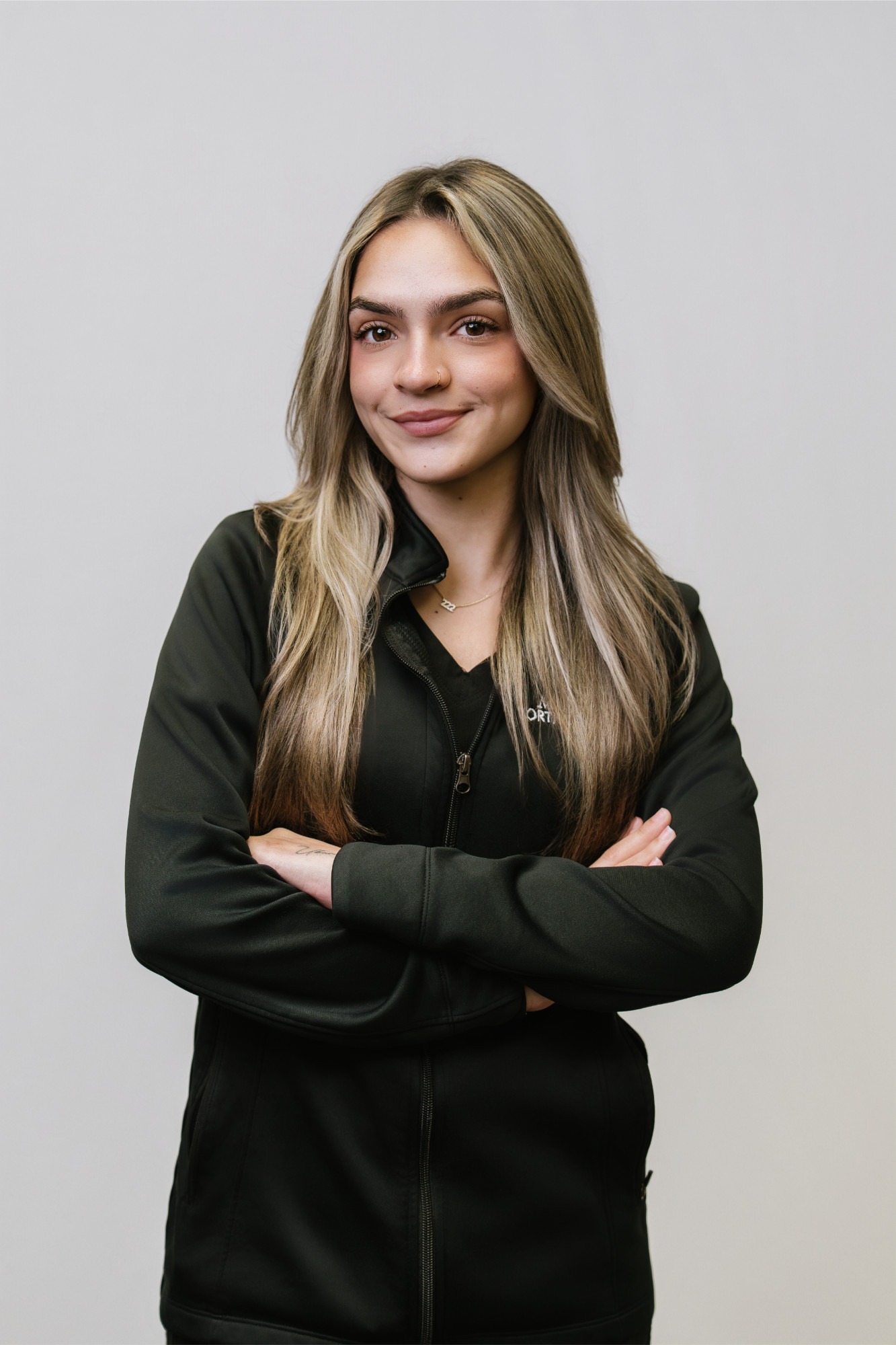 Clinical Assistant at Marris Orthodontics, smiling with arms crossed, wearing a black zip-up jacket, against a neutral background, representing the orthodontic team dedicated to providing braces and Invisalign in Orlando.