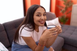 Young woman smiling while holding a cup, sitting on a couch, promoting orthodontic care and braces from Marris Orthodontics in Orlando.