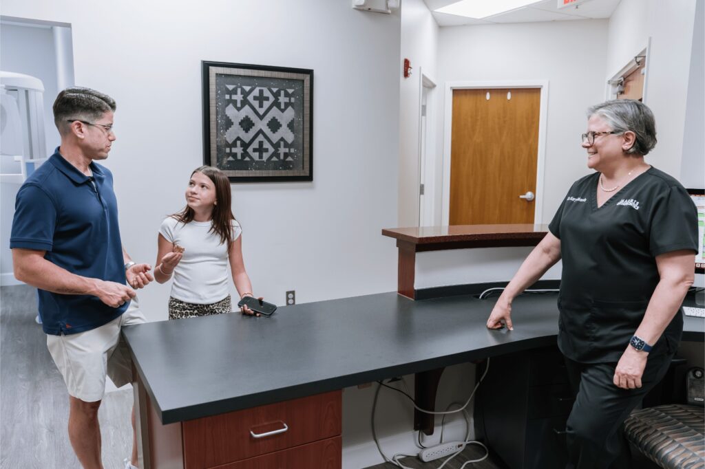 Dr. Kary Marris greets a father and his daughter at the front desk of Marris Orthodontics, her Orlando orthodontics office, before an appointment